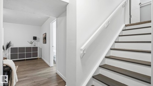 Modern entryway featuring a geometric black-and-white tile accent wall, wood-finish flooring, and a staircase with contrasting dark treads and white risers - 63 Rosemount Boulevard, Beaumont, AB - Indoor Photo Showing Other Room