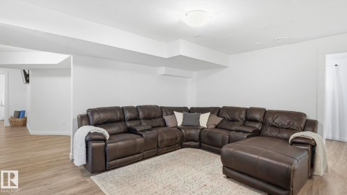 Expansive lower-level recreation room featuring a sectional layout with ample seating capacity, wood-finish flooring throughout, recessed ceiling lighting, and abundant natural light from multiple windows - 63 Rosemount Boulevard, Beaumont, AB - Indoor Photo Showing Living Room