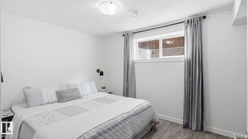 Bright bedroom featuring a large window with gray thermal curtains, wood-finish flooring, and recessed ceiling lighting - 63 Rosemount Boulevard, Beaumont, AB - Indoor Photo Showing Bedroom