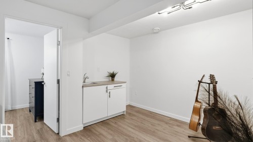 Modern studio space featuring a wood-finish plank floor, white cabinetry with integrated sink and countertop, recessed ceiling lighting, and abundant natural light from white-framed entry doors - 63 Rosemount Boulevard, Beaumont, AB - Indoor Photo Showing Other Room