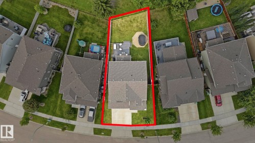 Aerial view showcasing a well-proportioned lot with mature landscaping, defined property boundaries, and a residential structure featuring a dark asphalt roof - 63 Rosemount Boulevard, Beaumont, AB - 
