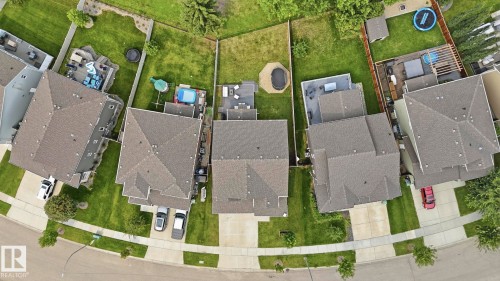 Aerial view showcasing a well-planned residential community with multiple single-family homes featuring pitched rooflines, manicured front and rear lawns, mature landscaping, and individual driveways with ample parking - 63 Rosemount Boulevard, Beaumont, AB -  With View