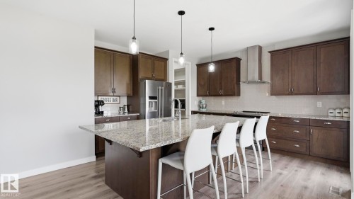Contemporary kitchen featuring dark wood cabinetry, quartz waterfall island countertop, stainless steel appliances, pendant lighting, and wood-finish flooring throughout the open-concept space - 63 Rosemount Boulevard, Beaumont, AB - Indoor Photo Showing Kitchen With Upgraded Kitchen