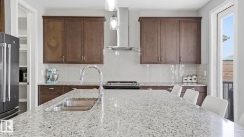 Sophisticated kitchen featuring custom wood-finish cabinetry, quartz countertops with waterfall edge detailing, stainless steel gas cooktop, and a contemporary pendant lighting fixture above the island - 63 Rosemount Boulevard, Beaumont, AB - Indoor Photo Showing Kitchen With Double Sink With Upgraded Kitchen
