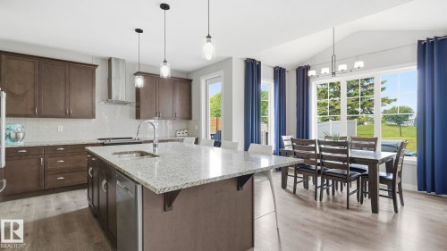 Open-concept kitchen and dining area featuring a large granite-topped island with pendant lighting, stainless steel appliances, dark cabinetry with quartz countertops, and hardwood flooring throughout - 63 Rosemount Boulevard, Beaumont, AB - Indoor Photo Showing Kitchen With Upgraded Kitchen