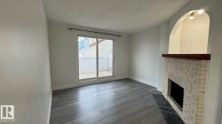 Light-toned wood-finish flooring, white brick fireplace with dark mantel, dark stone hearth, arched wall niche with overhead lighting, and sliding glass door to an outdoor patio - 