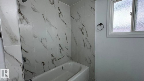 Full bathtub with a shower fixture, white tile surround with dark veining, and a frosted glass window - 41 Lancaster Terrace Nw, Edmonton, AB - Indoor Photo Showing Bathroom