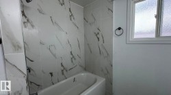 Full bathtub with a shower fixture, white tile surround with dark veining, and a frosted glass window - 