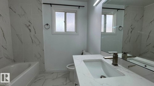 Bathtub with white tile surround, white vanity with integrated sink, contemporary faucet, and large wall-mounted mirror - 41 Lancaster Terrace Nw, Edmonton, AB - Indoor Photo Showing Bathroom