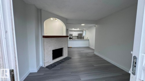 Living area featuring wood-finish flooring, a white brick fireplace with a wood mantle, and an arched pass-through to the kitchen with recessed lighting - 41 Lancaster Terrace Nw, Edmonton, AB - Indoor With Fireplace