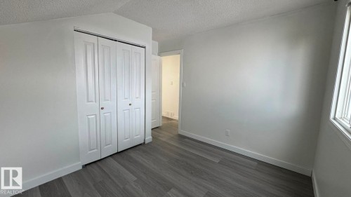 Light gray wood-finish flooring, white walls, white bi-fold closet doors with round brass hardware, white trim, and a window with blinds - 41 Lancaster Terrace Nw, Edmonton, AB - Indoor