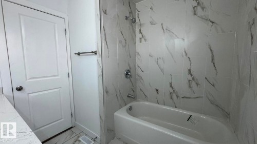 Bathtub with a shower, white and gray veined tile surround, chrome fixtures, and a white paneled door - 41 Lancaster Terrace Nw, Edmonton, AB - Indoor Photo Showing Bathroom