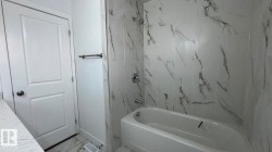 Bathtub with a shower, white and gray veined tile surround, chrome fixtures, and a white paneled door - 