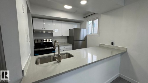 Kitchen featuring a stainless steel sink, contemporary faucet, white cabinetry, and light-toned countertops - 41 Lancaster Terrace Nw, Edmonton, AB - Indoor Photo Showing Kitchen With Double Sink