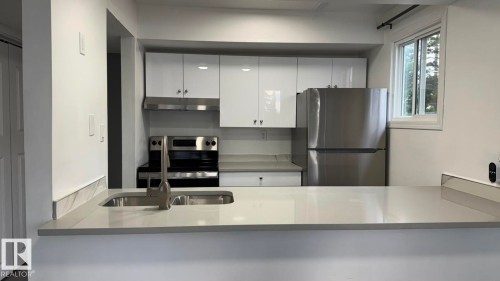 Integrated kitchen featuring white high-gloss cabinetry, stainless steel appliances, a double basin sink with a gooseneck faucet, and light-toned countertops - 41 Lancaster Terrace Nw, Edmonton, AB - Indoor Photo Showing Kitchen With Double Sink