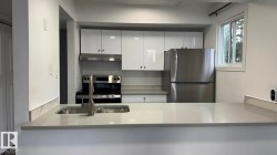 Integrated kitchen featuring white high-gloss cabinetry, stainless steel appliances, a double basin sink with a gooseneck faucet, and light-toned countertops - 