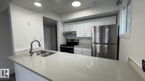 Kitchen featuring a dual basin sink with a gooseneck faucet, light-toned countertops, white cabinetry, and stainless steel appliances - 41 Lancaster Terrace Nw, Edmonton, AB - Indoor Photo Showing Kitchen With Double Sink With Upgraded Kitchen
