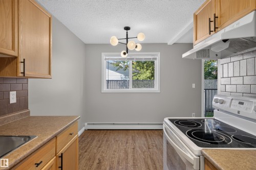 Wood-finish flooring, contemporary light fixture, updated cabinetry with modern hardware, and a white subway tile backsplash - #4 4616 47 St, Leduc, AB - Indoor Photo Showing Kitchen