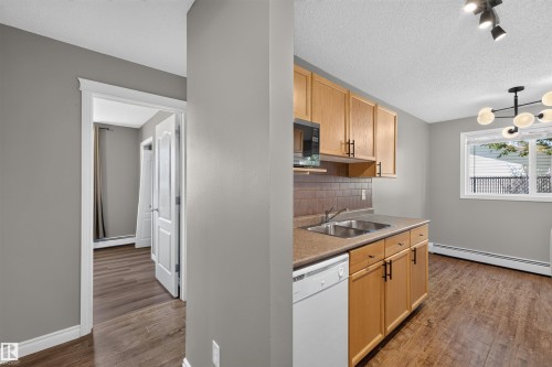 Open kitchen featuring wood-finish cabinetry, laminate countertops, stainless steel sink, and white subway tile backsplash - #4 4616 47 St, Leduc, AB - Indoor Photo Showing Kitchen With Double Sink