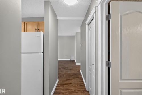 Efficient hallway layout with wood-finish flooring, white panel doors, recessed ceiling lighting, and a compact refrigerator with upper cabinetry for convenient access and storage - #4 4616 47 St, Leduc, AB - Indoor