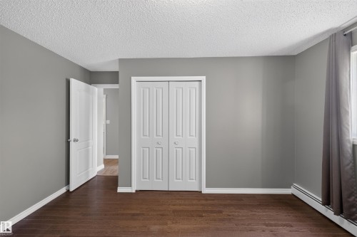 Dark wood-finish flooring with white trim, neutral gray walls, and white bi-fold closet doors - #4 4616 47 St, Leduc, AB - Indoor Photo Showing Other Room