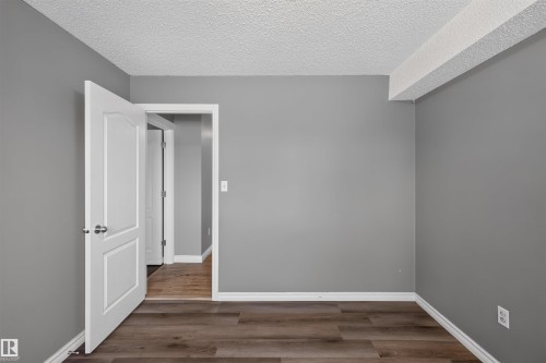 Neutral grey wall paint, wood-finish flooring, white baseboards, white panel door, textured ceiling - #4 4616 47 St, Leduc, AB - Indoor Photo Showing Other Room