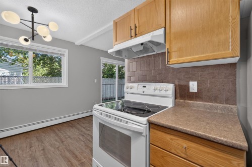 Wood-finish flooring, white window trim, contemporary ceiling light fixture, sliding glass patio door, and wood cabinetry - #4 4616 47 St, Leduc, AB - Indoor Photo Showing Kitchen