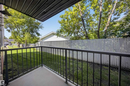 Private patio with concrete flooring and black metal railings, overlooking a fenced yard with mature trees - #4 4616 47 St, Leduc, AB - Outdoor With Exterior