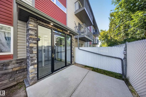 Stone veneer facade with red and beige siding, leading to a glass entry door, concrete patio, and chain-link fencing - #4 4616 47 St, Leduc, AB - Outdoor With Exterior