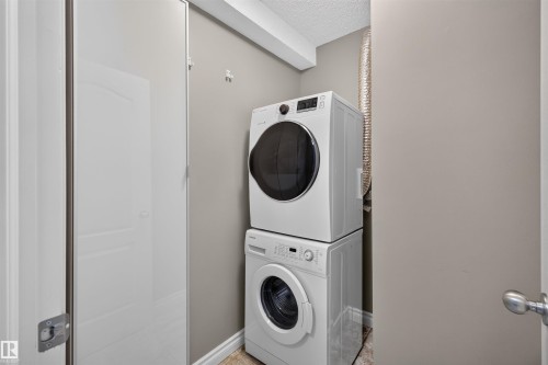 Stackable washer and dryer appliances, neutral wall paint, and wood-finish flooring - #4 4616 47 St, Leduc, AB - Indoor Photo Showing Laundry Room