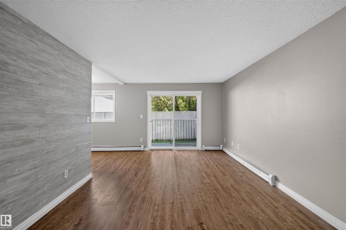 Wood-finish flooring throughout, light gray wall finishes, and a gray wood-finish accent wall - #4 4616 47 St, Leduc, AB - Indoor Photo Showing Other Room