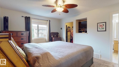 Spacious primary bedroom featuring a wood-finish bed frame, dual nightstands with drawer storage, ceiling fan with integrated lighting, carpeted flooring, and abundant natural light from large windows with blackout drapery hardware - 107 Hartwick Loop, Spruce Grove, AB - Indoor Photo Showing Bedroom