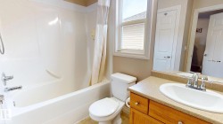 White bathtub with integrated shower, single-pane window, wood-finish vanity with a single sink, and mirror - 