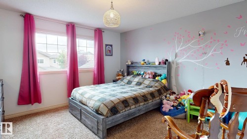 Bright secondary bedroom featuring large multi-pane windows with crimson curtains, neutral wall finishes, wood-finish flooring, and a pendant light fixture - 107 Hartwick Loop, Spruce Grove, AB - Indoor Photo Showing Bedroom