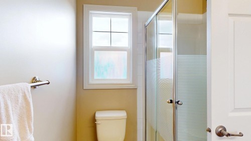 Compact bathroom featuring a glass-enclosed shower with frosted sliding doors, ceramic toilet, towel bar, and a window with cross-pane detailing providing natural light - 107 Hartwick Loop, Spruce Grove, AB - Indoor Photo Showing Bathroom