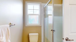 Compact bathroom featuring a glass-enclosed shower with frosted sliding doors, ceramic toilet, towel bar, and a window with cross-pane detailing providing natural light - 