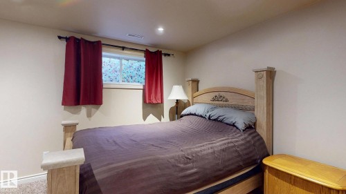 Comfortable bedroom featuring a wooden post bed frame, dark upholstered bedding, built-in wooden nightstands, burgundy window treatments, and recessed ceiling lighting - 107 Hartwick Loop, Spruce Grove, AB - Indoor Photo Showing Bedroom