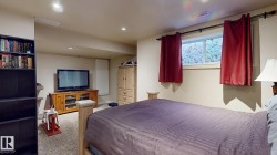 Spacious basement bedroom with plush carpeting, wood-finish entertainment cabinetry, and abundant natural light from high windows - 