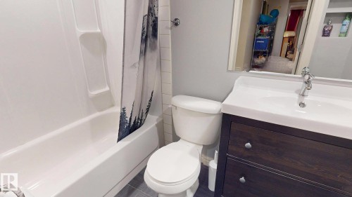 Full bathroom featuring a wood-finish vanity with dual drawers, white porcelain sink, and chrome faucet - 107 Hartwick Loop, Spruce Grove, AB - Indoor Photo Showing Bathroom