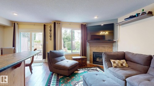 Open-concept living area featuring hardwood flooring, a gas fireplace with stone surround and mantel, comfortable seating arrangements, and abundant natural light from multiple glass doors and windows - 107 Hartwick Loop, Spruce Grove, AB - Indoor Photo Showing Living Room With Fireplace