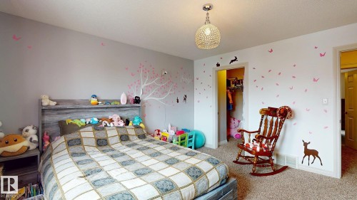 Spacious secondary bedroom featuring carpet flooring, generous natural light from multiple windows, built-in shelving with storage, pendant lighting fixture, and direct access to adjacent spaces - 107 Hartwick Loop, Spruce Grove, AB - Indoor Photo Showing Bedroom