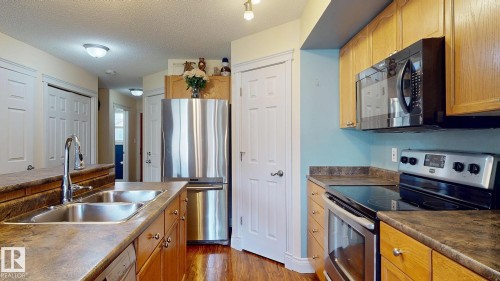 Kitchen featuring stainless steel appliances, wood-finish cabinetry, dual basin sink, and a built-in microwave - 107 Hartwick Loop, Spruce Grove, AB - Indoor Photo Showing Kitchen With Double Sink