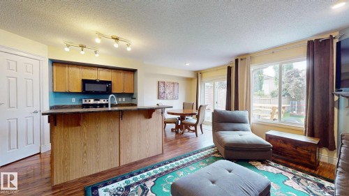 Open-concept living space featuring warm wood-finish cabinetry and countertops, stainless steel appliances, hardwood flooring, and abundant natural light from expansive windows and glass doors - 107 Hartwick Loop, Spruce Grove, AB - Indoor