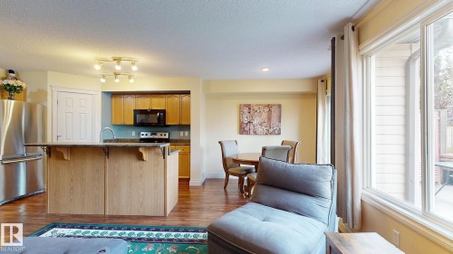 Kitchen island with an extended countertop, stainless steel appliances, wood-finish flooring, and a dining area - 107 Hartwick Loop, Spruce Grove, AB - Indoor Photo Showing Kitchen