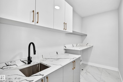 White upper cabinetry with gold-tone hardware, a stainless steel sink with matte black faucet, and patterned countertops - 233 Crystal Creek, Leduc, AB - Indoor Photo Showing Kitchen