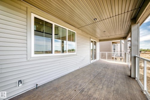 Covered porch featuring wood-finish flooring, white horizontal siding, multiple large windows with natural light exposure, wood-beamed ceiling, and glass railing details overlooking the surrounding landscape - 233 Crystal Creek, Leduc, AB - Outdoor With Deck Patio Veranda With Exterior