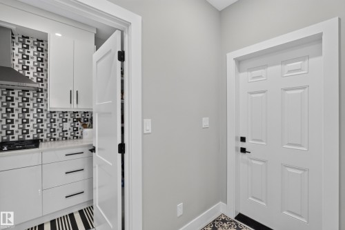 Modern kitchen featuring white cabinetry, a striking black and white geometric tile backsplash, and a stainless steel range hood - 4703 41 Street, Beaumont, AB - Indoor Photo Showing Other Room