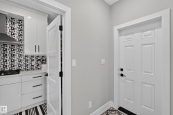 Modern kitchen featuring white cabinetry, a striking black and white geometric tile backsplash, and a stainless steel range hood - 