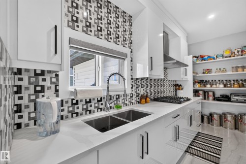 Contemporary kitchen featuring a dual basin sink, white countertops, sleek white cabinetry, a gas cooktop with a stainless steel range hood, and a custom tile backsplash - 4703 41 Street, Beaumont, AB - Indoor Photo Showing Kitchen With Double Sink With Upgraded Kitchen
