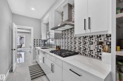 Modern kitchen featuring white cabinetry with sleek hardware, a gas cooktop, and a stainless steel range hood - 